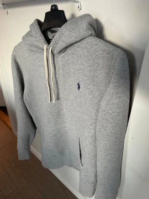 Grå hoodie från Polo Ralph Lauren - Snygg grå hoodie från Polo Ralph Lauren med klassisk broderad logga i mörkblått på bröstet. Tröjan är använd men i gott skick. Hör av er vid frågor!