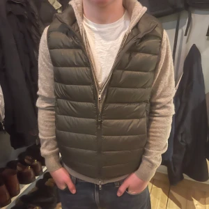 Mörkgrön pufferväst från Uniqlo - Snygg mörkgrön pufferväst med horisontella quiltade paneler och hel dragkedja framtill från Uniqlo. Västen har en clean look och passar perfekt över en hoodie eller t-shirt. Materialet är syntet och ger en lätt och skön känsla. Perfekt för dig som gillar streetwear och vill ha en chill stil.