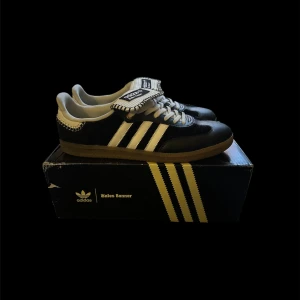 Adidas Samba Wales Bonner - Adidas Samba Wales Bonner sneakers i svart och vitt med klassiska tre ränder på sidan. Skorna har en unik, broderad detalj runt kanten och en gummisula. Tungan är extra stor med Wales Bonner-logga och randigt mönster. Materialmix av skinn och mocka, snörning framtill.