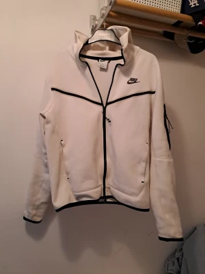 Nike zip upp hoodie från Nike. Size s.  - Stilren vit zip-hoodie från Nike med svarta detaljer. Perfekt både till vardags och träning. Modern passform med hög krage och hel dragkedja framtill. Praktiska fickor samt en extra ficka med dragkedja på ärmen. Mjukt och bekvämt material som håller formen fint. Size s men passar även M. Skriv gärna prisförslag