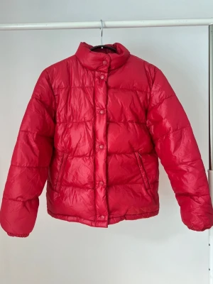 Röd pufferjacka med hög krage - Röd dunjacka från Amica. Jackan har en hög krage och stängs med knappar. Den har även fickor på sidorna. Storlek 36 <3