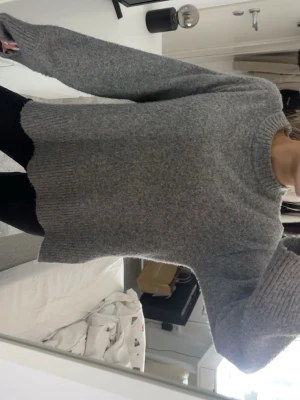 Grå stickad tröja med slits - Mysig grå stickad tröja med lång ärm och ribbade muddar. Tröjan har en rund halsringning och coola slitsar på sidorna vid nederkanten. Passformen är loose och materialet känns mjukt och värmande, perfekt för kyliga dagar.