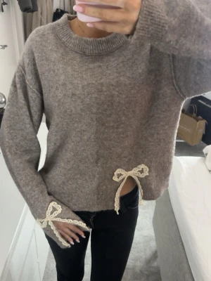 Beige stickad tröja med spetsrosetter - Superfin beige stickad tröja med lång ärm och söta spetsrosetter i offwhite vid ärmslut och ena sidan av midjan. Tröjan har en loose passform och ribbade muddar vid hals och nederkant. i storlek 164 men passar mej som har XS/S i vanliga fall!🤎