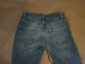 Blå bootcut jeans med klassisk tvätt - Säljer ett par low waist bootcut jeans från Subdued det har ett litet hål som går lätt att fixa. Skulle säga att det passar XS-S