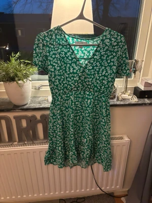 Grön klänning med blommor  - Grön klänning med vita blommor på, skick är svårt att sätta exakt då alla har olika åsikter men enligt mig är skicket bra och jag kan inte hitta några skador när jag kollar igenom