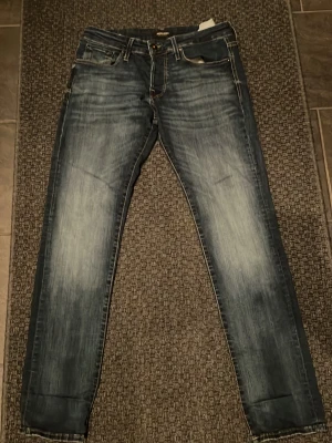 Blå slim jeans från Jack & Jones - Säljer ett par blå slim jeans från Jack & Jones med snyggt slitna detaljer och kontrastsömmar. Klassisk femficksmodell och normalhög midja. Jeansen har en tvättad look och är tillverkade i jeansmaterial med stretch. W 31 L 32