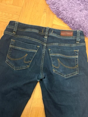 Mörkblå bootcut jeans från LTB - Snygga mörkblå jeans från LTB med klassisk bootcut-modell. Jeansen har kontrastsömmar i gult, fem fickor och läderpatch bak i midjan. Materialet är stretchigt jeans och passformen är normal. Perfekta för dig som gillar en tidlös look med lite utsvängda ben. 26/30