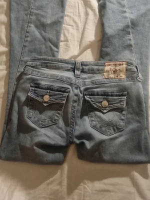 True Religion Joey Low Rise Flare Jeans - Säljer ett par ljusblå True Religion Joey jeans med LÅG midja och flare-ben. Klassiska snygga fickor med knappar. Köpta på carlings för 1299kr!