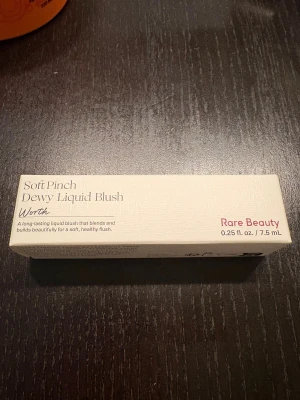 Rare Beauty Soft Pinch Dewy Liquid Blush - Rare Beauty Soft Pinch Dewy Liquid Blush i nyansen Worth. Flytande rouge som ger en fräsch, daggig finish och smälter in i huden. Kommer i en stilren beige kartong, 7,5 ml. Perfekt för att skapa en naturlig glow med enkel applicering.