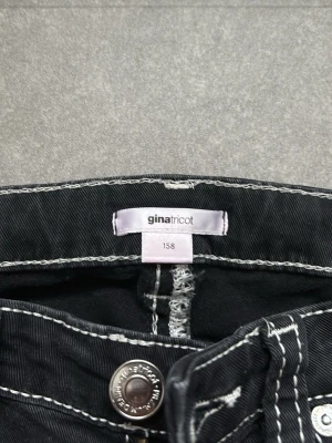 Svarta bootcut jeans från Gina Tricot - Säljer ett par svarta jeans från Gina Tricot i storlek 158. Byxorna har vita kontrastsömmar, broderade bakfickor och bootcut-ben. Klassisk femficksmodell med knapp och dragkedja framtill. Perfekta för dig som gillar en retrovibe! Jeans har använts 1 gång men finns inga synliga spår av användning.