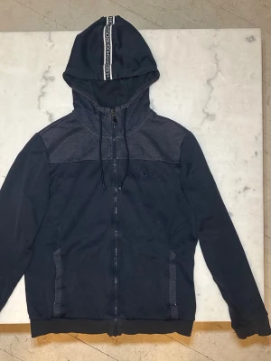 Mörkblå Hugo Boss Hoodie - Säljer en snygg mörkblå Hugo Boss hoodie i storlek S. Hoodien är i använt skick, finns tecken på användning. 