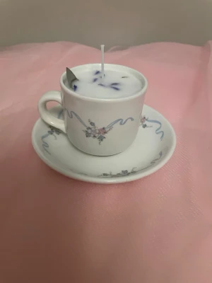 Doftljus av vaniljdoft i en vit tekopp med blommor och blåa streck nr 8 - Det här ljuset är gjort av återanvändbara material. Tekoppen är köpt secondhand och stearinet är från kyrkor som tänkte slänga det. Det här ljuset har en svag doft utav vanilj, så känsliga även kan använda det. Det här ljuset har även torkade blommor på som dekoration. Det finns fler av denna design på hemsidan om man vill köpa sets. 