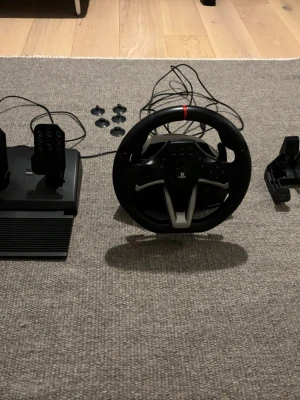 HORI Racing Wheel Apex - HORI Racing Wheel Apex för PlayStation med pedaler och fästen. Komplett set med USB-anslutning, kompatibel med PS4, PS5 och Dator. Ratt och pedaler i fint skick, inga synliga defekter eller slitage. Perfekt för realistisk racingupplevelse hemma.