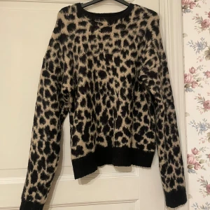 Leopardmönstrad stickad tröja NA-KD - Säljer en supermjuk stickad tröja från NA-KD med leopardmönster i svart och beige. Tröjan har rund halsringning, långa ärmar och ribbade muddar. Fint skick och perfekt till vintern då den är väldigt varm!