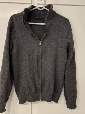 Mörkgrå stickad kofta från Hanstholm - Säljer en mörkgrå stickad kofta från Hanstholm med hel dragkedja framtill och ribbad hög krage. Passar S kanske lite mindre eller större. Tveka inte att skriva.