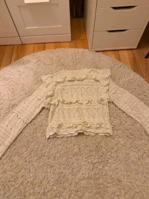 Vit stickad tröja med volanger - Supersöt vit stickad tröja med långa ärmar och volangdetaljer över bröstet och axlarna. Tröjan har ett genombrutet mönster och känns både romantisk och trendig. Perfekt till höst och vår för en extra stylish look. Säljer för att den har blivit för liten.
