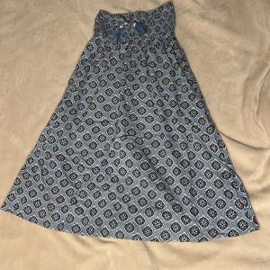 Vacker lång kjol - Säljer en extremt fin blå lågmidjad kjol med coolt mönster. Har fin rosett detalj med pärlor och stretchig midja. Ifrån Gina tricot I strl 146/152 vilket motsvarar en XXS. Perfekt för svenska sommardagar eller utomlandsresor. Aldrig använd. 