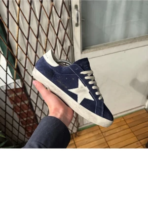 Blåa sneakers från Golden Goose - Säljer ett par blåa sneakers från Golden Goose med vit stjärndetalj på sidan och vita snören. Skorna har en klassisk mocka material. Skicket är 8/10 använda är dom ju. Inget og följer med bara skorna. Skriv vid frågor och funderingar.🙂