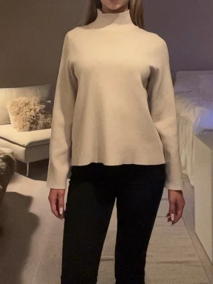 Beige polotröja med lång ärm - Snygg beige polotröja med lång ärm och rak passform. Tröjan har en hög hals och är tillverkad i ett mjukt material.