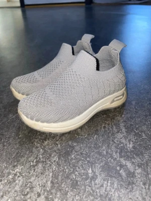 Grå stickade slip-on sneakers - Säljer ett par gråa  sneakers med vit sula. Skorna har en modern, sportig look 