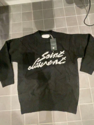 Svart stickad Saint Laurent tröja -   Säljer en Saint Laurent-tröja i helt nytt skick, aldrig använd. Originaltaggar kvar. Storlek S. Stilren och exklusiv design med hög kvalitet – perfekt för dig som vill ha något lyxigt och trendigt.