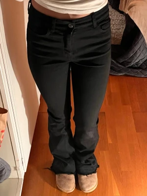 Svarta bootcut jeans high waist - Säljer ett par svarta jeans med bootcut-modell och råa, fransiga benslut. Byxorna har hög midja, klassiska fem fickor och stängs med knapp och dragkedja. Materialet är stretchigt jeans för en bekväm passform. Jag är 162 och dessa byxor når lite nedanför hälen på mig