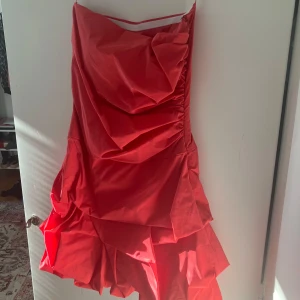Röd tub klänning från Jake*s - Snygg röd klänning från Jake*s med volangdetaljer. Perfekt för att sticka ut på festen. Klänningen har en axelbandslös stil som ger en elegant look.