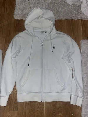 Vit Polo Ralph Lauren zip hoodie - Vit zip hoodie från Polo Ralph Lauren. Klassisk modell med broderad logga på bröstet. Skön och varm, funkar perfekt till vardags.  Använd men i okej skick. Finns fläckar/missfärgningar framtill (se bilder), därav priset. Inget som påverkar funktionen, men bra att veta.