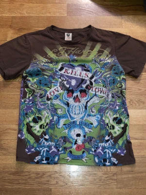 Vintage Ed Hardy T-Shirt Storlek L - Super get brun Ed Hardy tischa med deras klassiska dödskallar och kristaller på. Storleken på tvättlappen säger large, men enligt mig passar den någonstans emellan en medium och en smalare large.