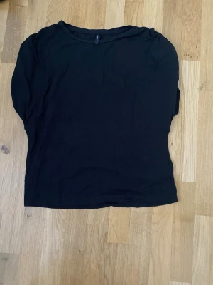 Svart långärmad topp från Peppercorn - En enkel och stilren svart långärmad topp från Peppercorn. Modellen har rund halsringning och är gjord i mjukt bomullstyg som känns skönt mot huden. Perfekt att matcha med jeans eller kjol för en clean look.