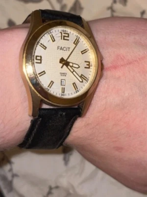 Ingen väst på bilderna - Bilderna visar en armbandsklocka från Facit med svart läderarmband och guldfärgat ur. Ingen väst syns på bilderna.