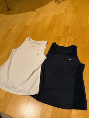 Fila Sportlinnen - Set om 2, Storlek L - Två sportlinnen från Fila. Ett i vitt och ett i mörkblått. Båda har meshdetaljer. Som nya!