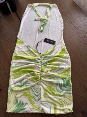 Grönvit mönstrad halterneckklänning - Grönvit  kort halterneckklänning från Nelly med swirlmönster i grönt, vitt och ljusgult. Aldrig använd. Storlek S