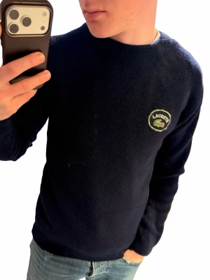 Lacoste ull tröja  - Riktigt fin tjock ull tröja från Lacoste i en marinblå färg. Väldigt fint skick utan några defekter. Är lite liten i storleken så passar XS/S skulle jag säga, har själv normalt S