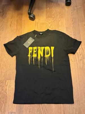 Fendi t-shirt - Svart t-shirt från Fendi med stor gul FENDI-logga framtill och FF-symbol på ryggen. T-shirten har klassisk passform, rund hals och är kortärmad. Tillverkad i mjuk bomull och har en cool streetkänsla med det droppade trycket.