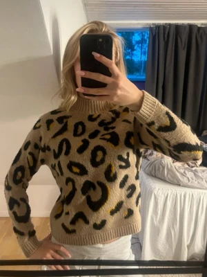 Beige leopard stickad tröja - Säljer en beige stickad tröja från Amisu i storlek XS. Tröjan har leopardmönster i svart och gult, hög krage och ribbade muddar. Skit snygg 💗