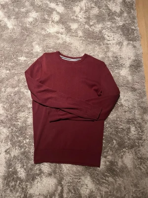 Mörkröd långärmad tröja - En stilren mörkröd tröja med rund halsringning och långa ärmar. Tröjan har ribbade muddar vid ärmslut och nederkant, perfekt för dig som gillar en enkel men snygg look. Passar till både jeans och kjol.