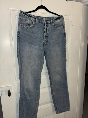 Ljusblå mom jeans H&M - Klassiska mom jeans från H&M i ljusblå tvätt med raka ben och knappgylf. Jeansen har fem fickor, bälteshällor och den ikoniska läderpatchen bak i midjan. Tillverkade i slitstarkt bomullsjeansmaterial och har en tidlös, avslappnad passform.
