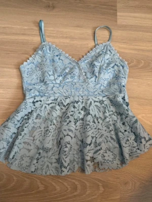 Ljusblå spetslinne med smala band - Supersöt ljusblå linnetopp med tunna axelband och v-ringning. Toppen har ett blommigt spetslager över ett mjukt innerfoder och en lätt utsvängd passform. Perfekt för sommarens alla tillfällen och ger en romantisk vibe. På sista bilden kan man se att jag har klippt ut vaddering men det är inget som syns på utsidan! Köptes för 250kr på en marknad! Den är en onesize men passar bäst en S/M