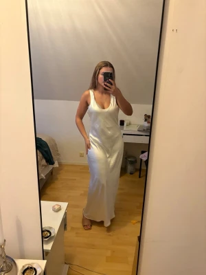 Vit långklänning i satin från Bik Bok - Supersnygg vit långklänning från Bik Bok i glansigt satinmaterial. Klänningen är ärmlös med djup urringning fram och rundad rygg. Perfekt för sommarens alla tillfällen och ger en elegant look. Aldrig använd då den är för stor på mig. Superfin till balen eller kanske studentmottagningen elelr finare evenemang! Säljes med prislapp kvar nypris 600kr! 