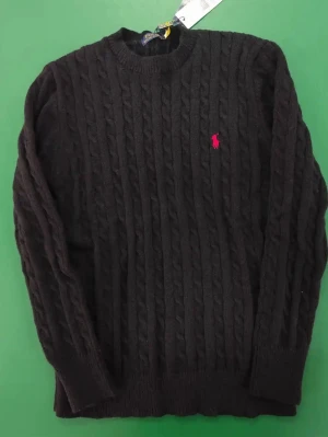 Svart kabelstickad tröja från Polo Ralph Lauren - Svart kabelstickad tröja från Polo Ralph Lauren med rund hals och lång ärm. Klassisk design med röd broderad logga på bröstet. Tröjan är gjord i mjukt material och har ribbade muddar vid ärmslut och nederkant. Perfekt för dig som gillar stilrena och tidlösa plagg.