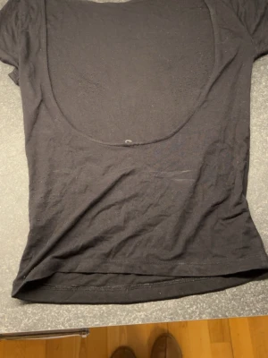 Svart tight topp med öppen rygg - Säljer en svart topp i stretchigt material med korta ärmar och stor, rundad öppen rygg. Toppen är tight och smickrande, perfekt till jeans eller kjol. Enkel och stilren design utan mönster eller detaljer. Alla lappar är bortklippta. 