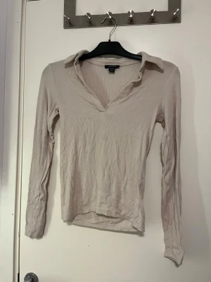 Beige ribbad långärmad topp Amisu - Säljer en beige ribbad långärmad topp från Amisu i storlek S. Toppen har en snygg krage och v-ringning som ger en clean look. Materialet är mjukt och stretchigt, perfekt till jeans eller kjol. Enkel att styla och passar till många olika outfits. Väldigt snygg på men använd fåtal gånger. Pris kan alltid diskuteras!🤗