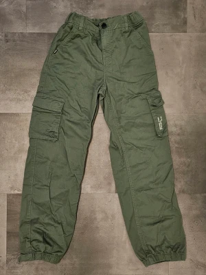 Cargopants - Säljer ett par gröna cargopants från Kappahl i storlek 158 men de passar även size S. Byxorna har flera praktiska fickor på sidorna, resår i bensluten och klassisk cargostil. Perfekta för dig som gillar en avslappnad och funktionell look.