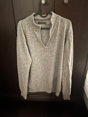 Grå stickad half zip-tröja Oscar Jacobson - Snygg grå stickad tröja från Oscar Jacobson med half zip-dragkedja och ribbad krage. Tillverkad i Italien, storlek L men sitter mer som M. Perfekt för dig som gillar stilrena och bekväma plagg med lite sportig touch. Passar till jeans eller chinos. 