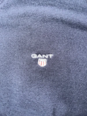 Mörkblå stickad tröja från GANT - Snygg mörkblå stickad tröja från GANT med v-ringad hals och broderad logga på bröstet. Tröjan har långa ärmar och ribbade muddar vid ärmslut och nederkant. Perfekt för dig som gillar klassisk stil och vill ha något som funkar året runt.passar dig 155/165