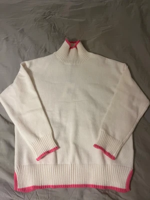 Vit polotröja med rosa detaljer från ”meet me there”💕 - Säljer en vit polotröja med ribbad hög krage och långa ärmar, aldrig använd. Tröjan har stickad struktur och snygga rosa kanter vid krage, ärmslut och nederkant. Perfekt för dig som gillar enkla men färgglada detaljer.