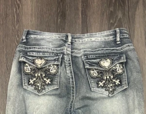 Blå bootcut mexikanska jeans - Snygga blå bootcut jeans med coola broderade detaljer och diamanter på bakfickorna. Jeansen har mellan midja och är tillverkade i klassiskt polyester material så de är mer stretchbara än hårda jeans Perfekta för dig som vill sticka ut med unika detaljer på dina jeans.