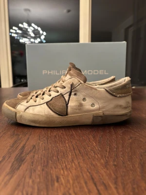 Philippe Model  sneakers  - Snygga sneakers från Philippe Model i beige och brunt med detaljer i mocka och canvas.  Klassisk design med logga på hälen och sidorna. Perfekta för dig som gillar en avslappnad och trendig stil. Dom ändå defekterna på skorna är på sulan där de har gått upp det gör absolut att laga. Hör av dig vid minsta fråga eller fundering(pris går absolut att diskutera!) Mvh Hugo!