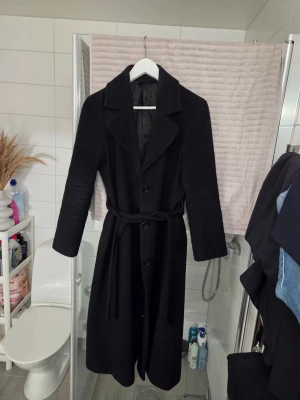 Svart ullkappa från & Other Stories - Säljer en lång svart ullkappa från & Other Stories Paris Atelier med snygg krage, knappar och bälte i midjan. Kappan har klassisk siluett och är tillverkad i italienskt tyg från Pontetorto. Perfekt för dig som gillar stilrena och tidlösa plagg. Nypris 3499kr 